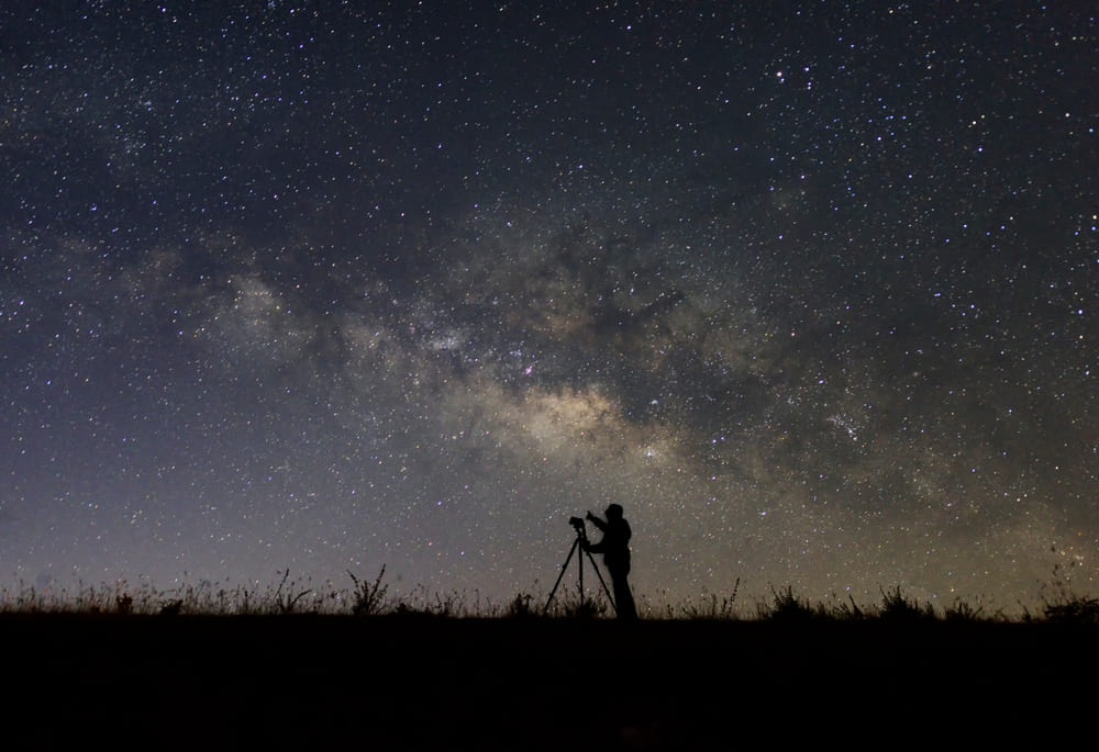 Mann mit Kamera vor einem funkelnden Sternenhimmel | Luminar Neo Blog

