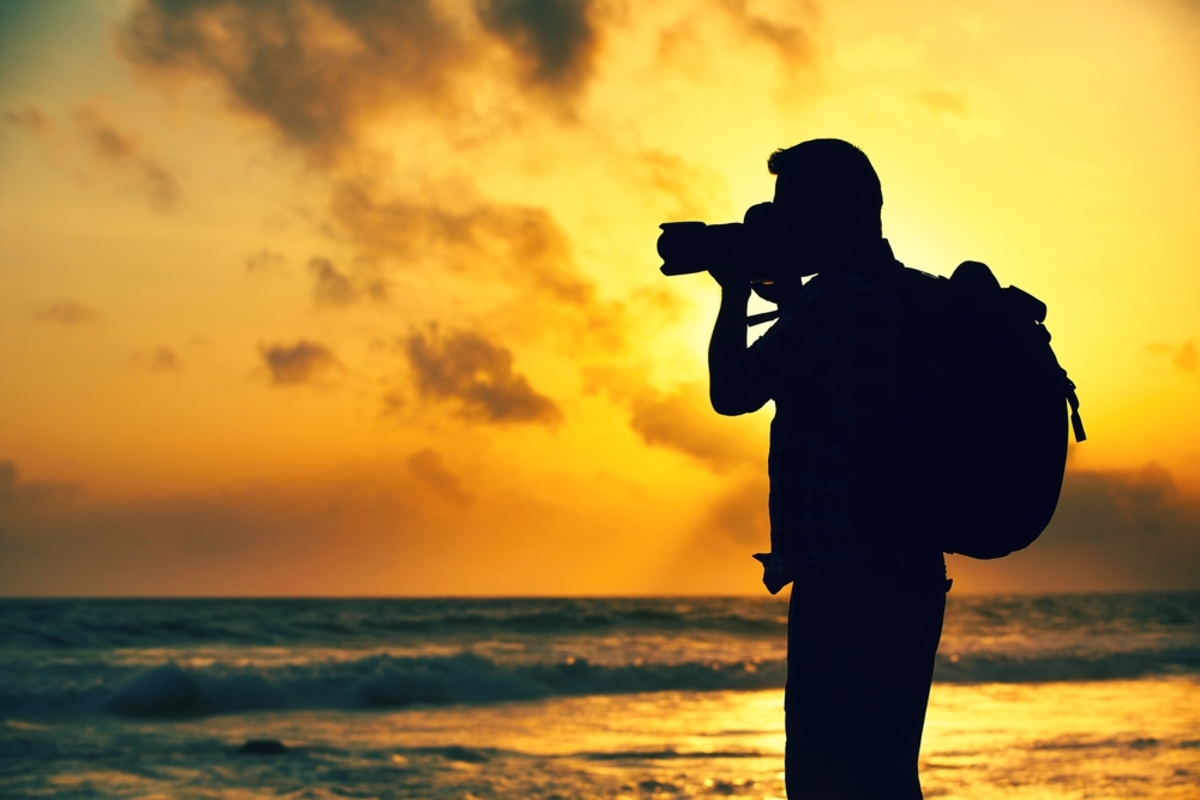Fotograf mit Rucksack fotografiert Sonnenuntergang am Meer | Luminar Neo Blog

