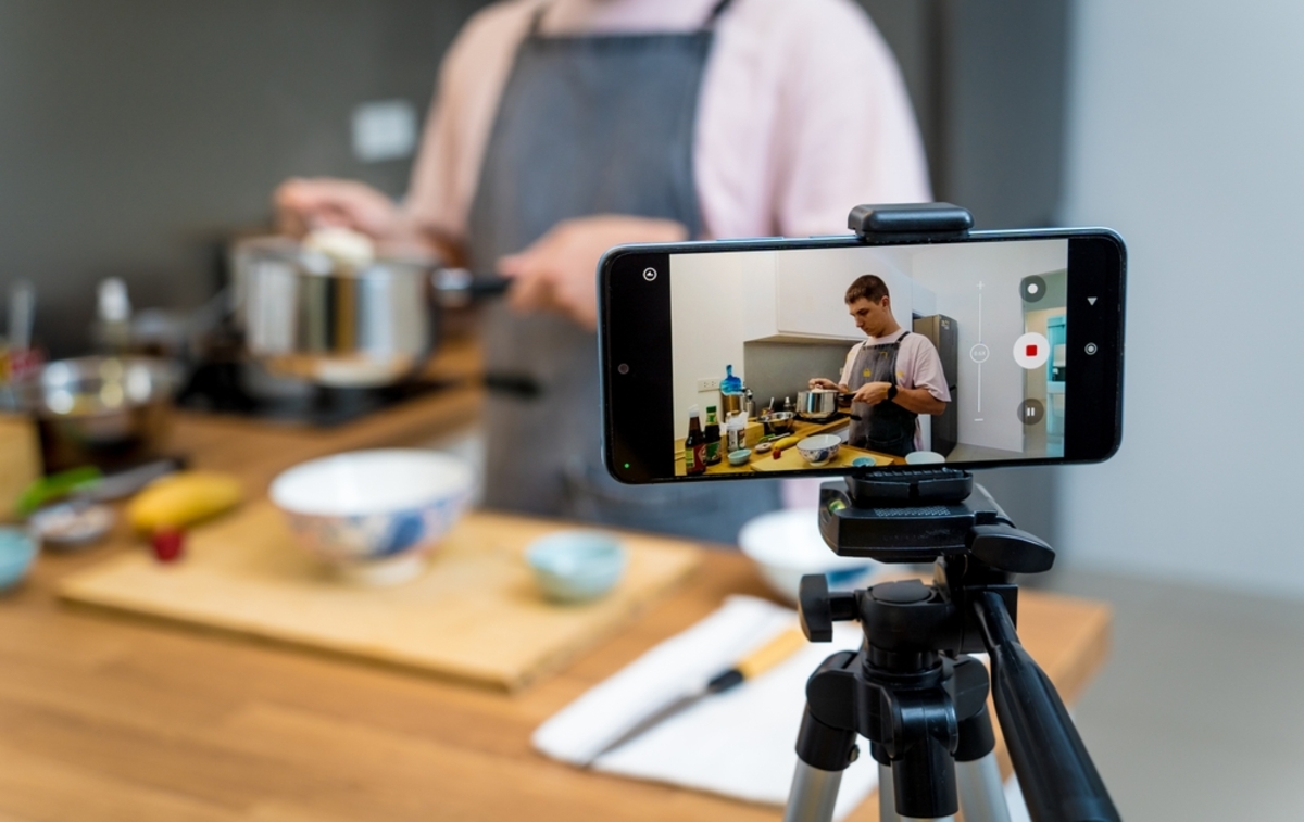 Ein Telefon auf einem Stativ nimmt ein Video von einem Mann auf, der Essen kocht | Luminar Neo Blog