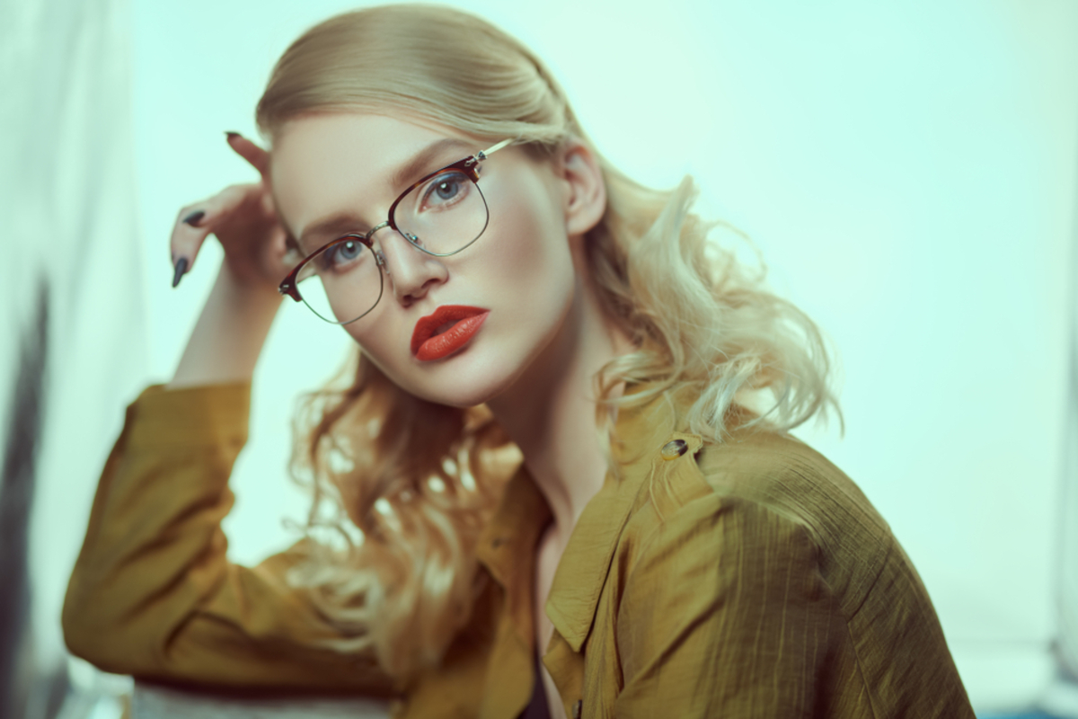 Blonde Frau mit Brille und roten Lippen in senfgelber Bluse, Hand am Kopf, Studioporträt | Luminar Blog