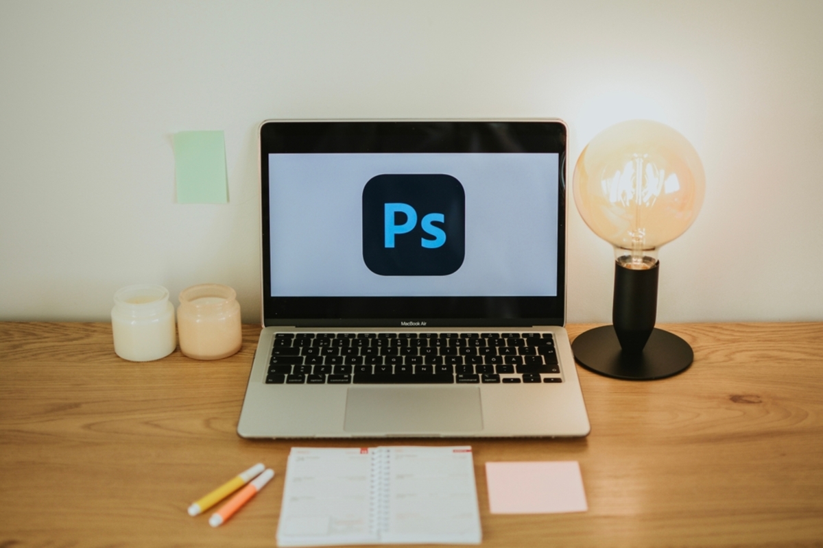 MacBook mit Photoshop-Logo auf dem Bildschirm neben Glühbirnenlampe auf Holztisch | Luminar Blog